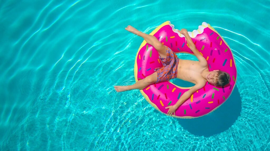 Aerial view of a child lounging on a donut float in a clear blue swimming pool.