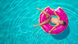 Aerial view of a child lounging on a donut float in a clear blue swimming pool.