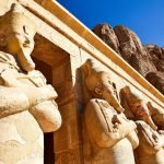 Ancient Egyptian statues at Hatshepsut Temple in Luxor under a clear blue sky.