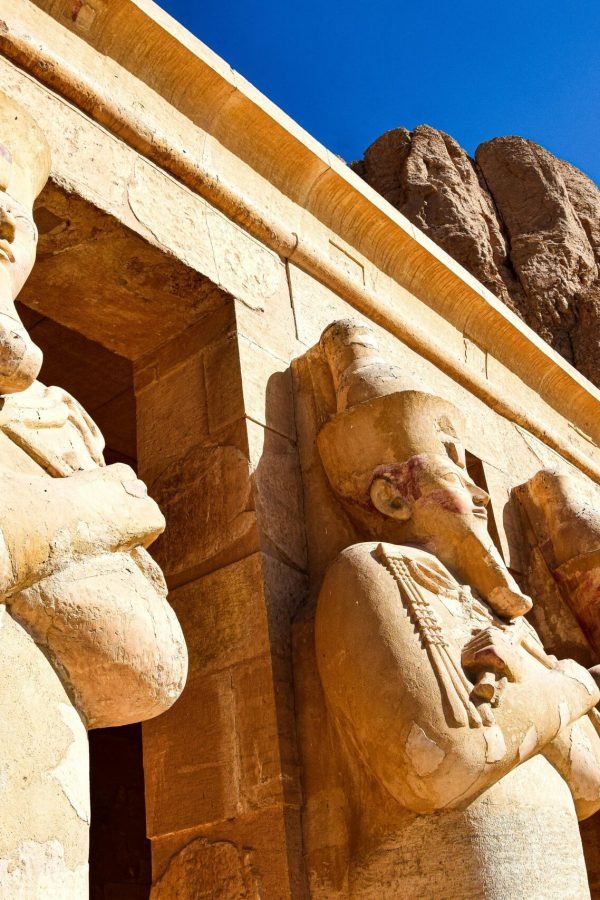 Ancient Egyptian statues at Hatshepsut Temple in Luxor under a clear blue sky.