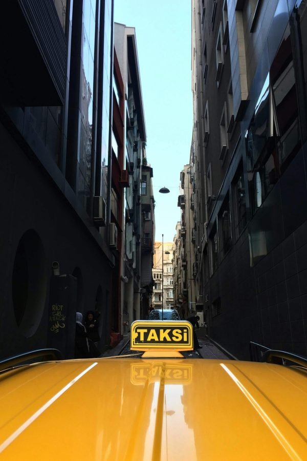 A yellow taxi navigates a narrow urban alley with tall buildings on either side, showcasing city life.