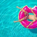 Aerial view of a child lounging on a donut float in a clear blue swimming pool.